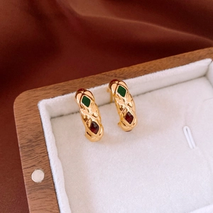 Close-up of golden C-shaped hoop earrings with vintage texture and colorful enamel stones
