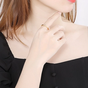 Détail d'une bague croix dorée avec zircons sertis, portée par un mannequin sous la lumière