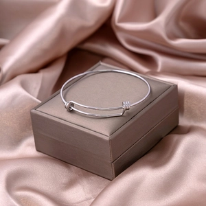 Close-up of silver minimalist knot bangle on brown jewelry box with silk fabric