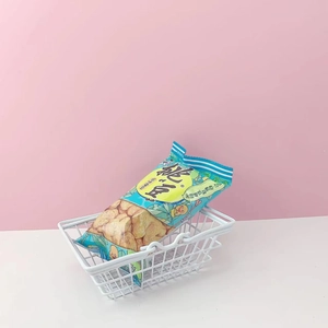 Close-up of white wire metal mini storage basket with snacks on pink and white background