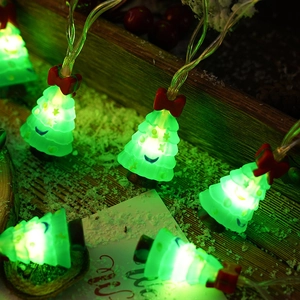 Close-up of green LED Christmas tree string lights with red bows on a snowy wooden surface