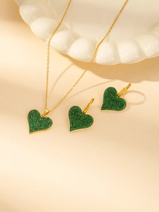 Dettaglio di parure dorata con collana e orecchini con cuori incastonati di pietre verdi