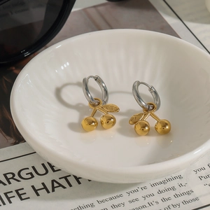 Detail of gold cherry pendant earrings on white ceramic plate with stylish background