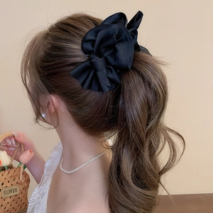 Detail view of a large black satin bow hair clip styled on a woman's hair in profile