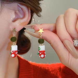 Close-up of Christmas snowflake pearl earrings with green velvet ball and red boots