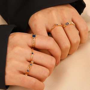 Close-up of five-piece gold ring set with blue gemstones worn on model fingers