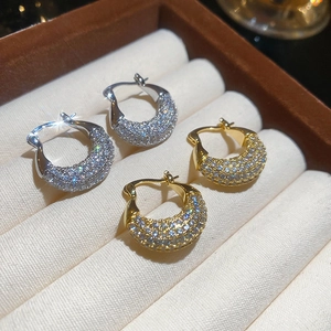Close-up of gold and silver pavé zircon huggie earrings in a luxury jewelry display box