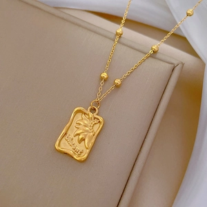 Minimalist gold titanium necklace with rectangular floral pendant on beige tray