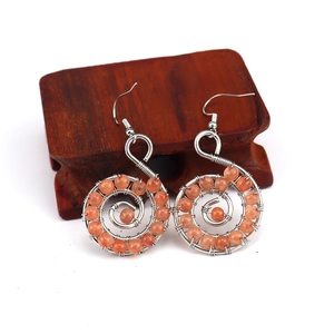 Detail of handmade spiral wire earrings with orange crystal beads on wooden base