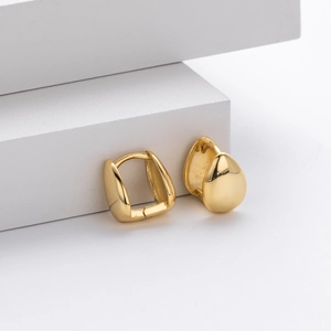 Macro detail of golden teardrop earrings displayed on minimalist white geometric props