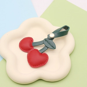 Detail of red PU leather cherry keychain with metal clasp on a white cloud tray