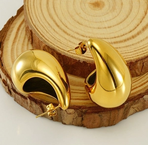 Polished gold teardrop earrings displayed on a natural wooden block with warm lighting