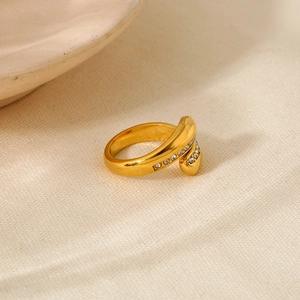 Detailed view of gold spiral crossover ring with white zircon pave on beige fabric