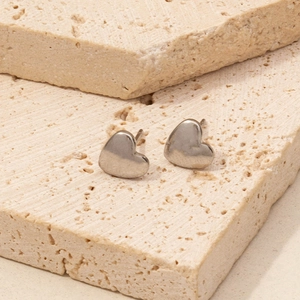 Close-up of polished silver heart earrings on a natural beige textured stone background