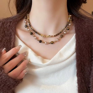 Detail of layered brown bead and pearl necklace worn with a brown cardigan
