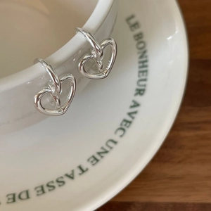 Minimalist S925 sterling silver heart-shaped hoop earrings hanging on a white ceramic cup
