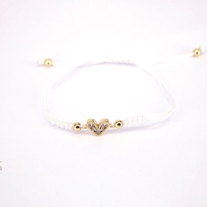 Detail of white braided bracelet featuring a gold heart charm with pavé cubic zirconia