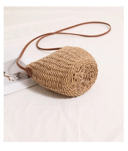 Detailed close-up of straw bucket bag texture and slim leather strap on white linen
