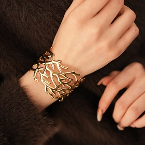 Detailed view of wide gold coral-textured cuff bracelet on a model wearing a brown sweater