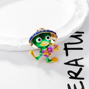 Cute green enamel frog brooch with blue hat and guitar accessory on white tray