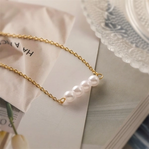 Macro shot of four white pearls on a delicate gold link chain over a soft background