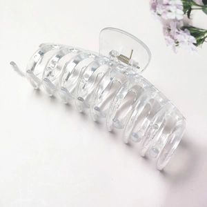 Detail view of transparent acrylic hair claw clip with silver spring on white table