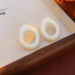 Close-up of minimalist cream resin hoop earrings on a textured fabric display tray