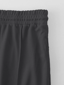 Detail of dark grey waffle knit tracksuit pants showing elastic waistband and stitching