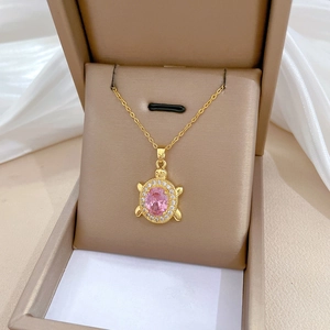 Macro detail of gold turtle pendant with pink stone and crystals on jewelry box