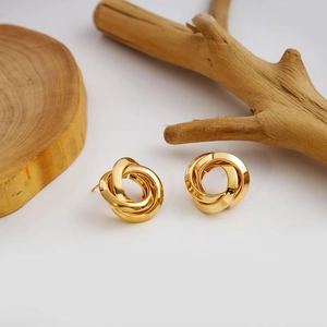Detail shot of golden knotted metal earrings with high-polish finish on natural wood background