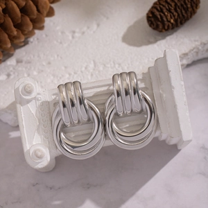 Detail of silver geometric hoop earrings with vertical stripes on a white Roman column