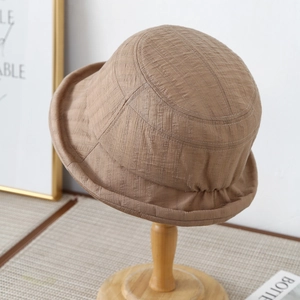 Detail of light brown bucket hat with fine fabric texture and rolled edge on wooden stand