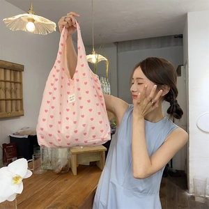 Close-up of pink canvas tote bag featuring vibrant red heart prints and top handles