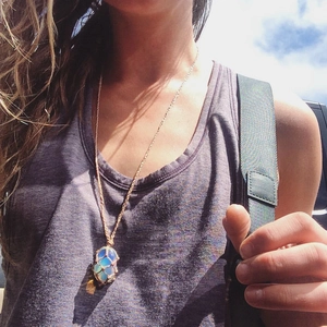 Blue opal crystal pendant in a woven gold chain mesh pouch necklace worn by a model