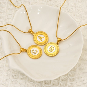18K gold plated shell alphabet necklace in white ceramic bowl with fabric backdrop