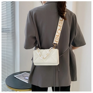 Detail of white quilted crossbody bag with woven jacquard strap and gold chain handle