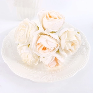 Macro view of realistic cream artificial rose heads on elegant white ceramic plate
