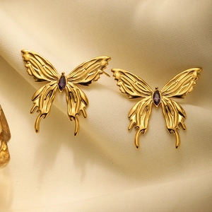 Detail of 3D butterfly earrings in gold finish with purple gemstones on soft cloth