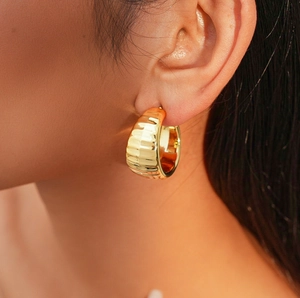 Detailed view of model wearing chunky golden C-shaped hoop earrings with vertical texture