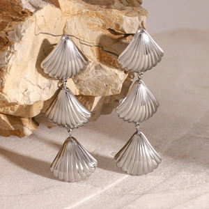 Polished stainless steel triple shell dangle earrings displayed on a natural rock background