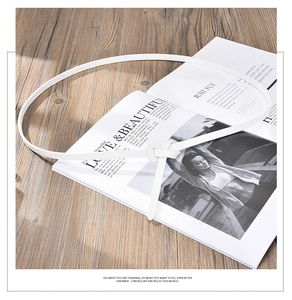 Detail of white slim faux leather waist belt tied on an open fashion magazine
