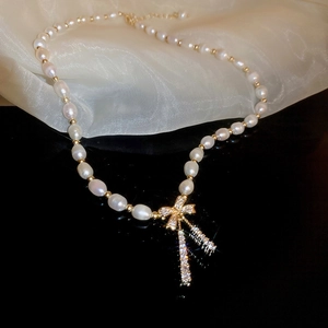 Elegant gold bow necklace with heart-shaped tassel pearls on a silk surface