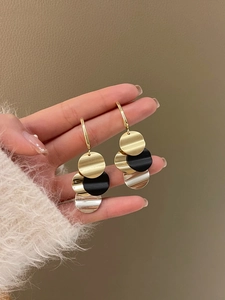 Detail view of multi-layer geometric metal disc earrings with gold and black finish