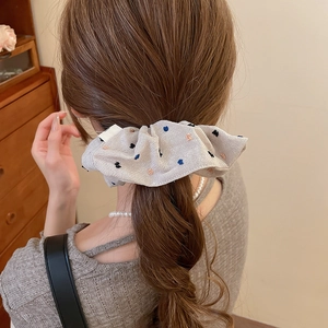 Detail of a large fabric scrunchie with colorful dots worn in a high ponytail