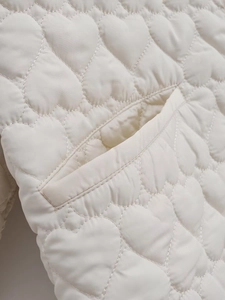 Detail of heart-shaped quilting and side pocket on a cream-colored puffer jacket