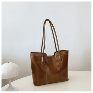 Deep brown tote bag with white contrast stitching detail on a minimalist white desk
