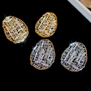 Détail de boucles d'oreilles ovales dorées et argentées serties de zircons rectangulaires