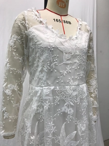 Detail of white lace wedding dress featuring floral embroidery and sheer long sleeves