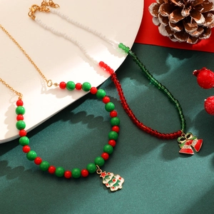 Détail d'un collier de Noël en perles avec breloques sapin et cloche sur fond vert