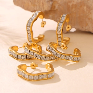 Golden wavy hoop earrings with square cubic zirconia on beige textured stone